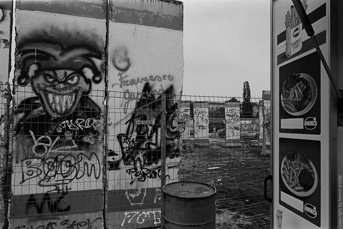 Dokumentarfotografie – Narr auf Berliner Mauer neben einer Imbisbude – Stadtportrait